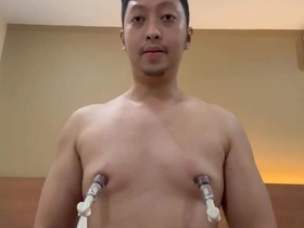 Young and Asian man with a naked body uses nipple pumps to enhance his pleasure.